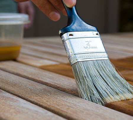 applying a coat of teak oil to the surface of a patio table top
